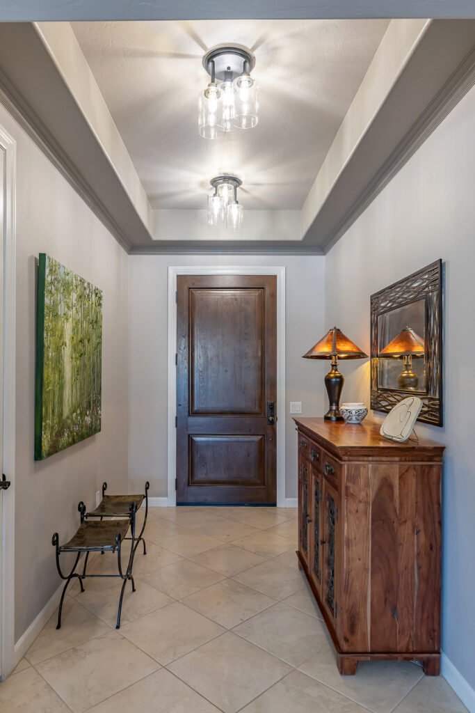 Gray paint two colors on tray ceiling and walls green art, mesquite furniture, mirror, dark wood entry door, glass and black ceiling lights, tiffany style lamp